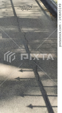 A spiked metal fence casts a linear shadow on a paved walkway. A spiked metal fence casts a linear shadow on a paved walkway. 143643149