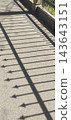 A spiked metal fence casts a linear shadow on a paved walkway. 143643151