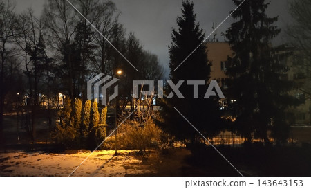 An autumn park at dusk with illuminated lanterns, colorful trees, and fallen leaves covering the paths. An autumn park at dusk with illuminated lanterns, colorful trees, and fallen leaves covering the paths. 143643153