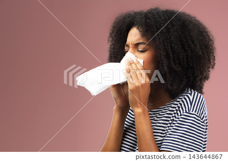 Blowing, nose and tissue with black woman in studio for sick or illness with allergies isolated on pink background. Flu, covid and virus with strain or infection with cold, sinus and sneezing. Blowing, nose and tissue with black woman in studio for sick or illness with allergies isolated on pink background. Flu, covid and virus with strain or infection with cold, sinus and sneezing. 143644867