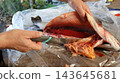 The process of cleaning a fresh salmon on a sheet of clear plastic film. Male hands slit open the fish's belly with a kitchen knife, removing the entrails and a large, mature skein of bright red roe. 143645681