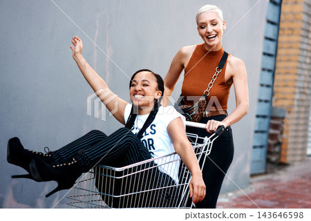People, girls and fun in trolley outdoor with laughing for funny adventure, playing and bonding on sidewalk. Friends, women and push cart in road with freedom, confidence and weekend break in city 143646598