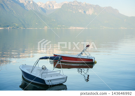 Two small moored boats on calm alpine lake water with peaceful mountain reflections Two small moored boats on calm alpine lake water with peaceful mountain reflections 143646992