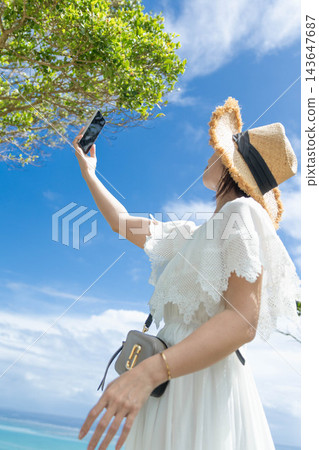 一名女子在沖繩的藍天下用智慧型手機自拍。 143647687