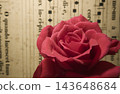 Close-up of a red rose with sparkling water droplets against an antique sheet music background. 143648684