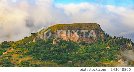 Sunlit highland plateau rises above drifting clouds with rugged cliffs and lush green slopes 143648860