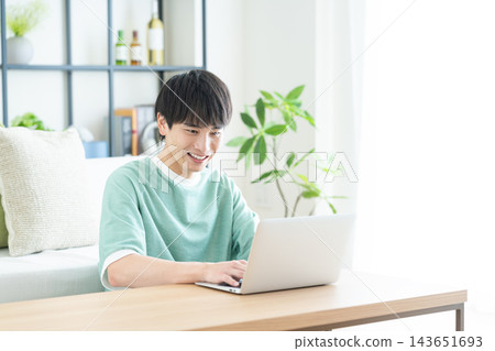 在客廳裡使用電腦的年輕人 在客廳裡使用電腦的年輕人 143651693