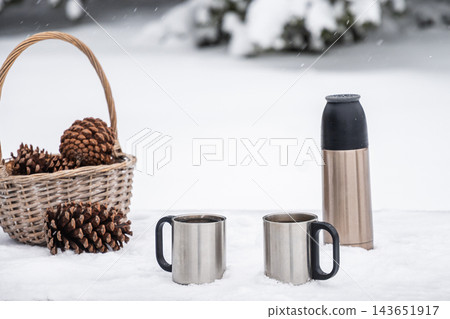 Two metal mugs and thermos in snow with pine cones Two metal mugs and thermos in snow with pine cones 143651917
