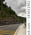 Winding mountain highway passing rocky cliff under cloudy sky 143651962