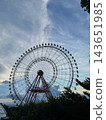 Ferris wheel rising above green trees against a cloudy sky 143651985