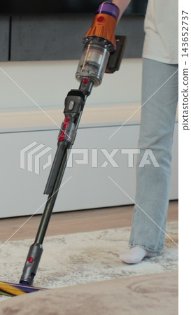 Vertical video. Young woman cleaning carpet with vertical vacuum cleaner in the house. House cleaning concept. Cleaning service. Vertical video. Young woman cleaning carpet with vertical vacuum cleaner in the house. House cleaning concept. Cleaning service. 143652737