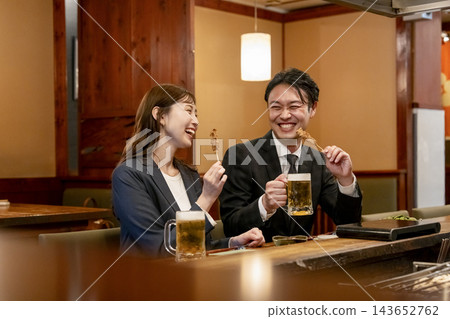 一男一女在吧台座位上享用烤雞串和啤酒。 一男一女在吧台座位上享用烤雞串和啤酒。 143652762