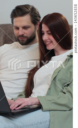 Vertical video. Couple uses a laptop computer on the floor of their apartment. Man and woman are talking, shopping on the Internet, choosing a product. 143652838