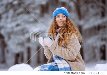Smiling woman with a thermos in a snowy forest enjoying nature. Adventure concept. Lifestyle. 143654110
