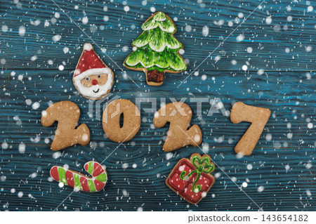 Festive gingerbread cookies for Christmas and New Year 2027 with spices and decorations on a dark wooden table 143654182