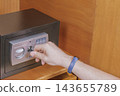 Close up of hand inserting emergency key into keyhole of small black digital safe inside wooden cabinet for unlocking during emergency situation 143655789