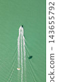 Top down aerial shot of speed motorboat towing parasail activity leaving white foam wake on turquoise sea surface with parachute shadow on water 143655792