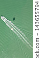 Top down aerial shot of speed motorboat towing parasail activity leaving white foam wake on turquoise sea surface with parachute shadow on water 143655794