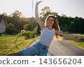 Smiling young woman dancing with raised arms on a quiet country road at sunset. Emotional wellbeing playful adulthood and joyful freedom 143656204