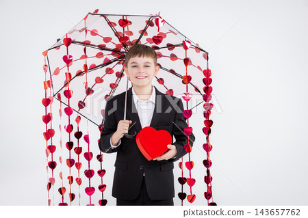 Boy dressed formally holds heart-shaped box and transparent umbrella  143657762
