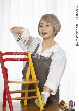 一位老婦人在客廳裡製作椅子,這是她的DIY愛好。 一位老婦人在客廳裡製作椅子,這是她的DIY愛好。 143658073