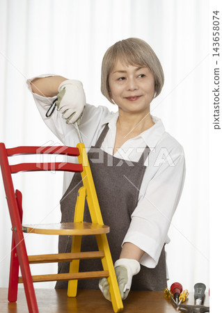 一位老婦人在客廳裡製作椅子,這是她的DIY愛好。 一位老婦人在客廳裡製作椅子,這是她的DIY愛好。 143658074