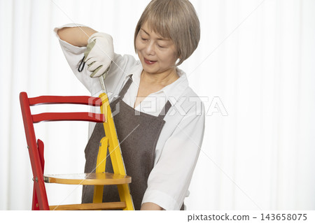 一位老婦人在客廳裡製作椅子,這是她的DIY愛好。 一位老婦人在客廳裡製作椅子,這是她的DIY愛好。 143658075
