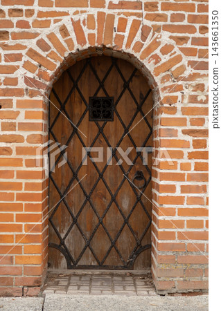 Rustic wooden door features a diamond pattern and wrought iron accents, framed by a brick wall, highlighting traditional architectural details Rustic wooden door features a diamond pattern and wrought iron accents, framed by a brick wall, highlighting traditional architectural details 143661350