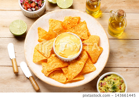 Crispy tortilla nachos on a rustic plate with creamy cheddar cheese sauce and guacamole, on a wooden table. Crispy tortilla nachos on a rustic plate with creamy cheddar cheese sauce and guacamole, on a wooden table. 143661445