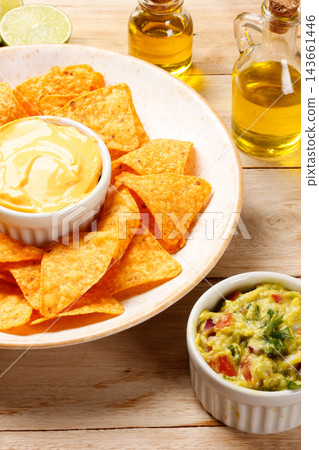 Crispy tortilla nachos on a rustic plate with creamy cheddar cheese sauce and guacamole, on a wooden table. Crispy tortilla nachos on a rustic plate with creamy cheddar cheese sauce and guacamole, on a wooden table. 143661446