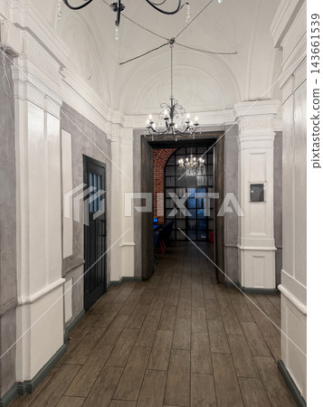 Elegant hallway features decorative molding and chandelier lighting, leading to a modern office space with a contrasting brick wall Elegant hallway features decorative molding and chandelier lighting, leading to a modern office space with a contrasting brick wall 143661539