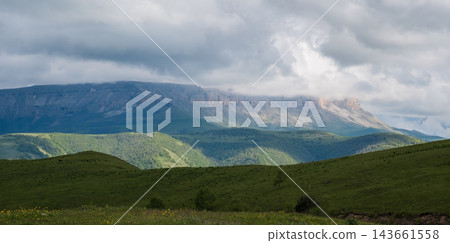Scenic landscape featuring rolling green hills and distant mountains beneath a cloudy sky, showcasing the beauty of nature in a rural setting 143661558