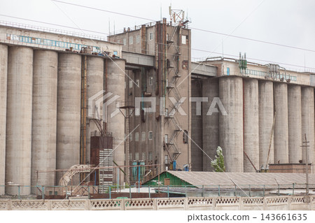 Industrial grain storage facility featuring tall concrete silos and a metal staircase, with a green structure visible in the foreground 143661635