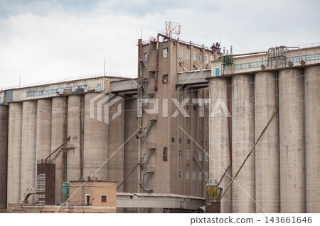 Industrial grain storage facility features large silos and exterior staircases, set against a cloudy sky in an urban landscape 143661646