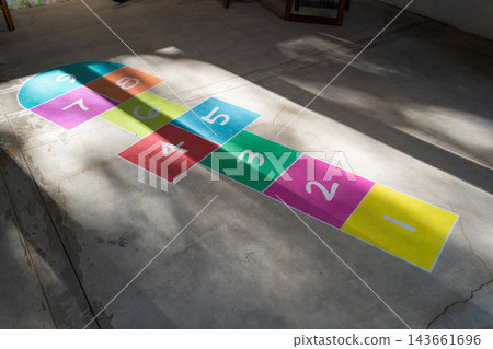 Colorful hopscotch game with numbers painted on concrete floor illuminated by sunlight and shadows 143661696
