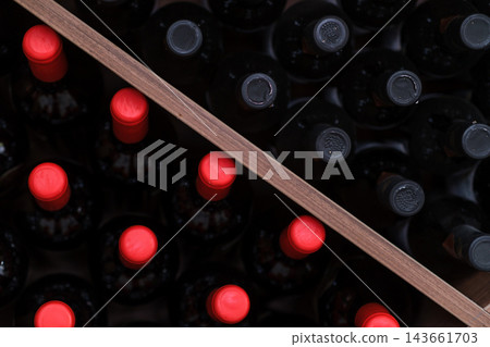 Top view shows dark bottles with bright red closures beside bottles with dark closures, separated diagonally by a wooden divider in storage Top view shows dark bottles with bright red closures beside bottles with dark closures, separated diagonally by a wooden divider in storage 143661703