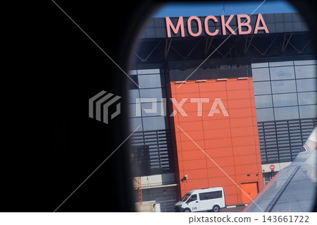 View from airplane window showing Moscow airport terminal with prominent signage, modern design, and a vehicle parked in front of the building 143661722