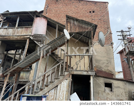 Tbilisi, Georgia - September 01, 2026: Aging wooden balconies and stairways surround a weathered brick building with satellite dishes, utility wires, and cloudy sky Tbilisi, Georgia - September 01, 2026: Aging wooden balconies and stairways surround a weathered brick building with satellite dishes, utility wires, and cloudy sky 143661741