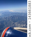 Airplane wing and engine section fill the foreground while layered rugged mountains and distant snowy peaks stretch beneath a clear blue sky 143661883