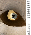 Round earthen shaft descends into darkness around a smaller central opening, revealing rough soil walls and a sunlit sandy surface 143661887