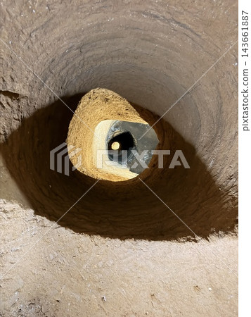 Round earthen shaft descends into darkness around a smaller central opening, revealing rough soil walls and a sunlit sandy surface Round earthen shaft descends into darkness around a smaller central opening, revealing rough soil walls and a sunlit sandy surface 143661887