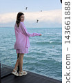 Woman wearing a pink striped outfit stands on a wooden dock above turquoise water, with seabirds flying near a calm coastal horizon 143661888