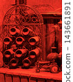 Red lighting reveals an ornate metal rack filled with rolled objects, a bottle, and a small toy tractor on a wooden shelf 143661891