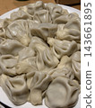 Numerous pale dumplings with folded pleated wrappers are piled together on a white plate, creating a close view of prepared food 143661895