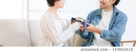 一位日本妻子在客廳沙發上送給丈夫禮物；丈夫接過禮物時，這對幸福的夫妻臉上洋溢著笑容。 （無臉） 143662018