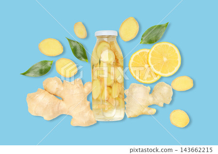 Sliced ginger and lemon surround a glass bottle filled with ginger tea 143662215