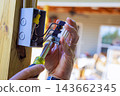 An electrician uses screwdriver to test wiring in an open electrical box inside building. 143662345