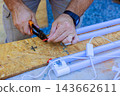 Electrician use pliers to cut red wire on a board beside fluorescent light fixture outdoors. 143662611