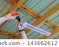 Hands connect wires to suspended fluorescent light beneath timber roof, indoors during repair. 143662612