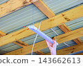 Professional electrician hand holds fluorescent tube under timber beams corrugated metal roof inside shed. 143662613